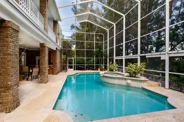 Voluminous pool screen enclosure has a spiral stairway leading to the master bedroom balcony